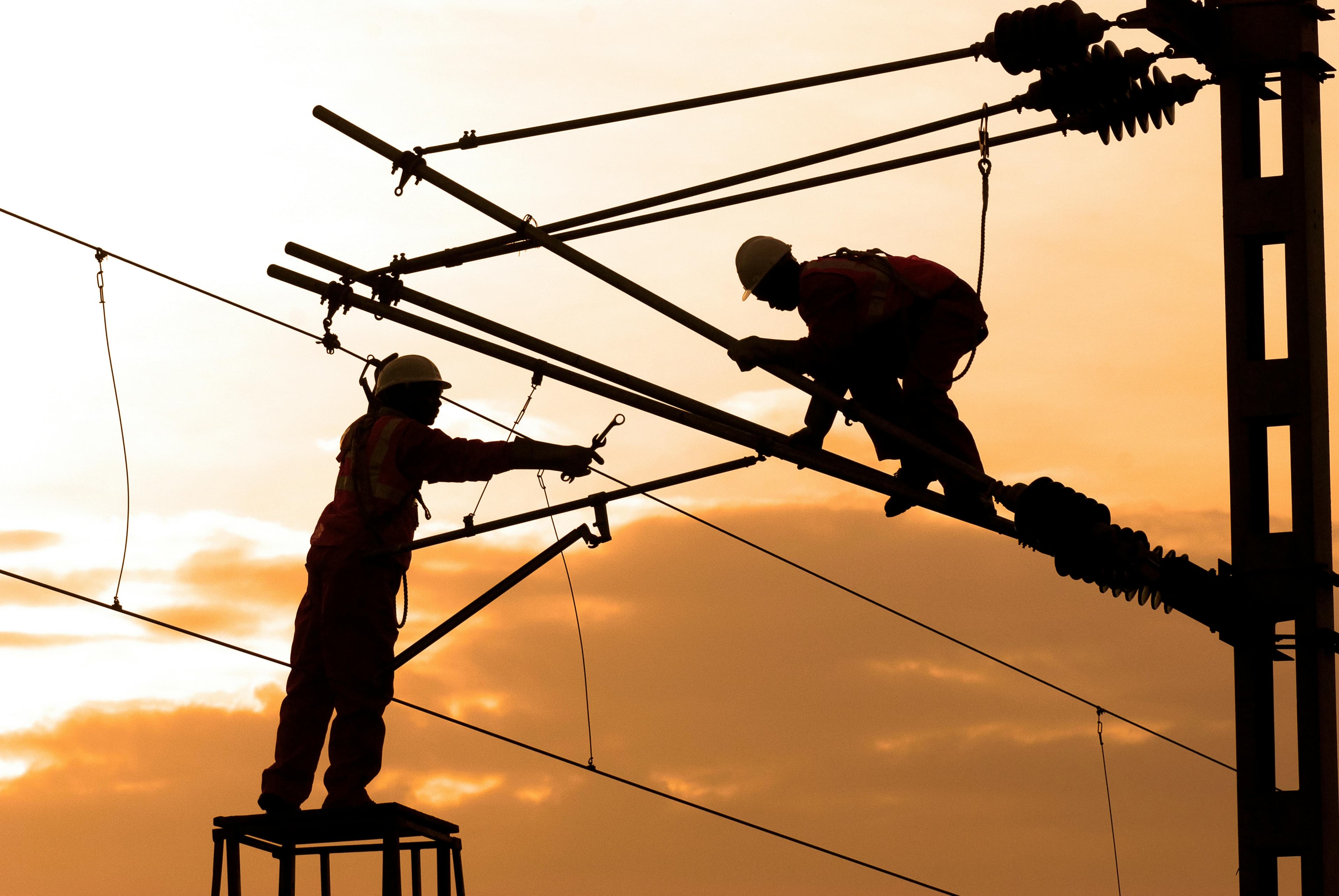 Linemen maintaining power lines at sunset